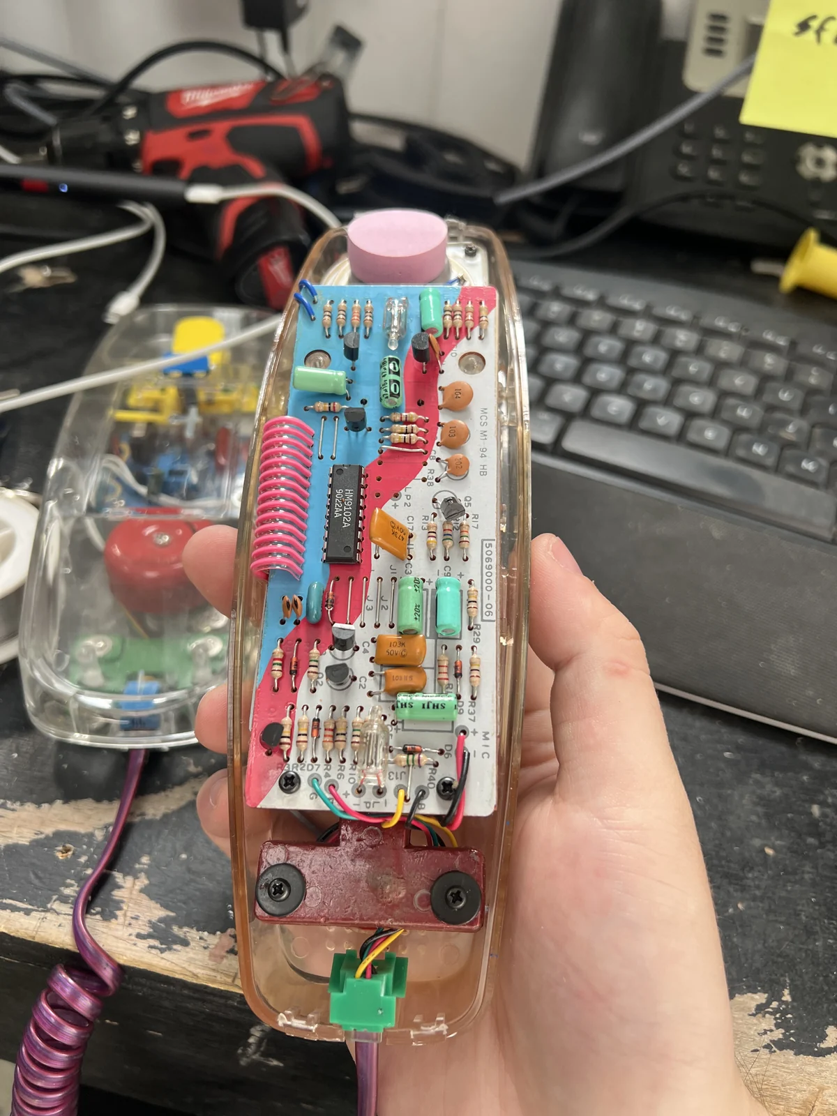 A hand holds the transparent telephone handset, revealing its circuit board
