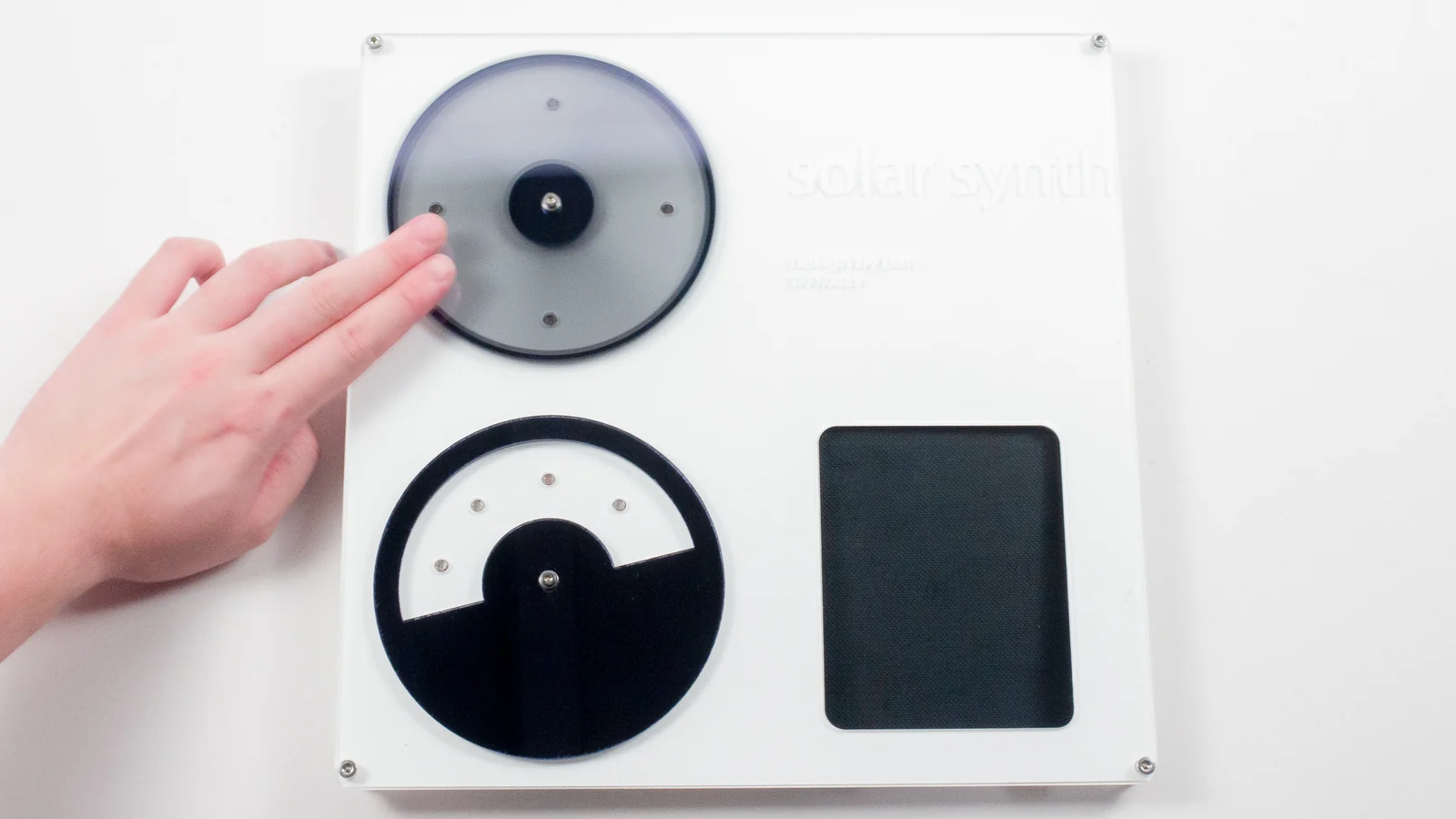 A hand plays the circular controls of a square solar synthesizer