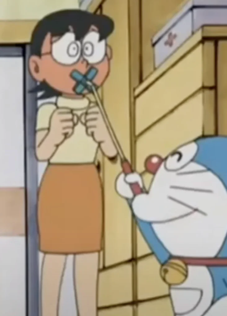 Doraemon holding the original cartoon gadget in front of a character’s mouth